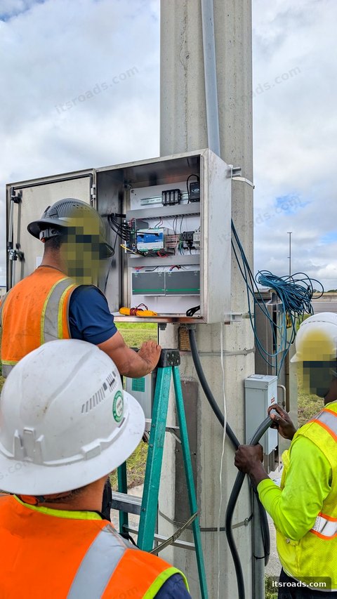 Technicians in hard hats at an open pole-mounted cabinet